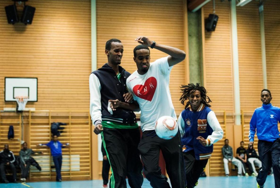 Killar spelar fotboll i en gymnastiksal.