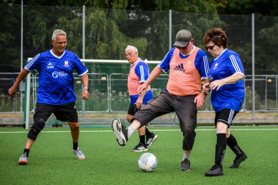 Äldre män och en kvinna spelar gåfotboll.